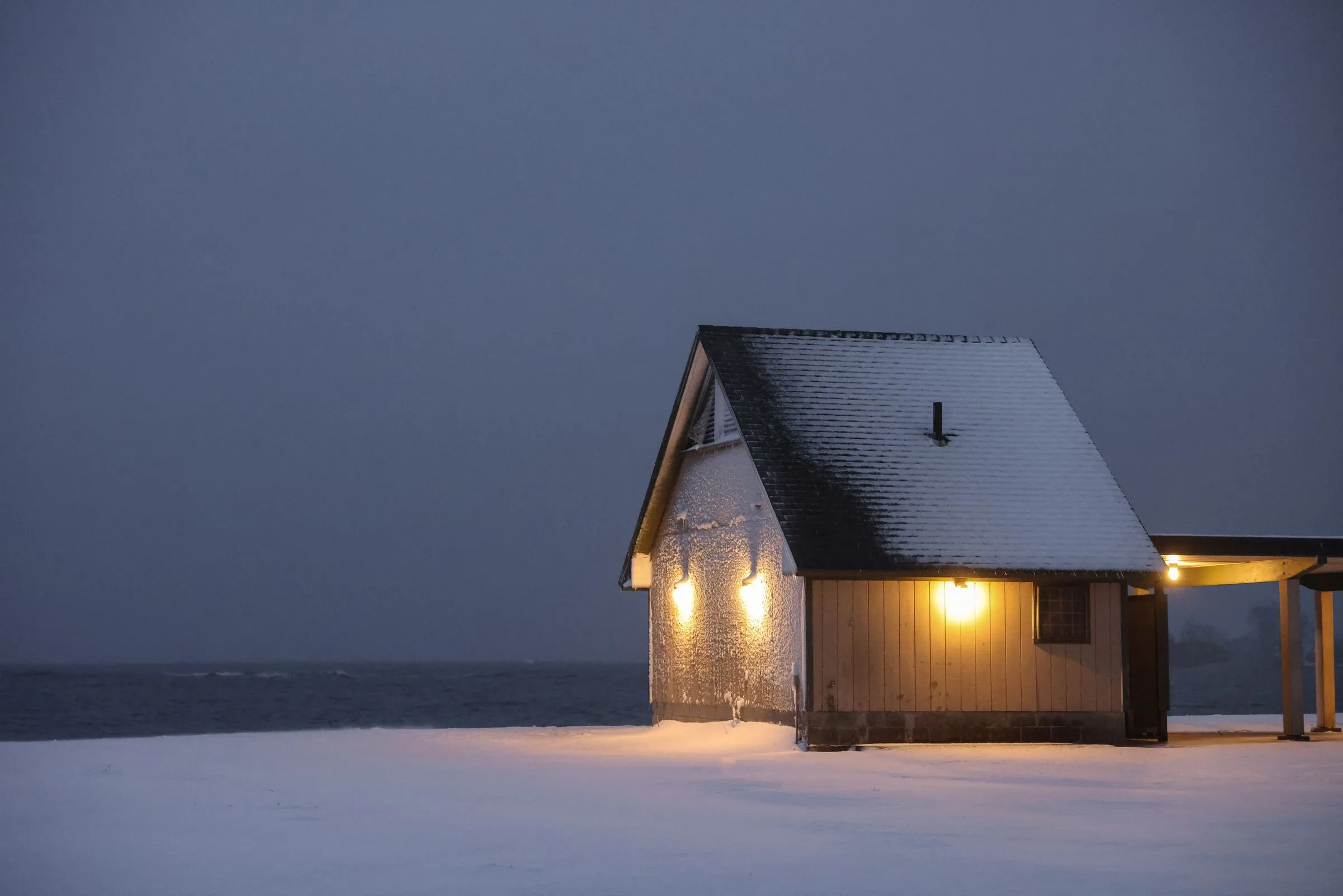 A small house with warm lights in the windows, in deep snow at dusk