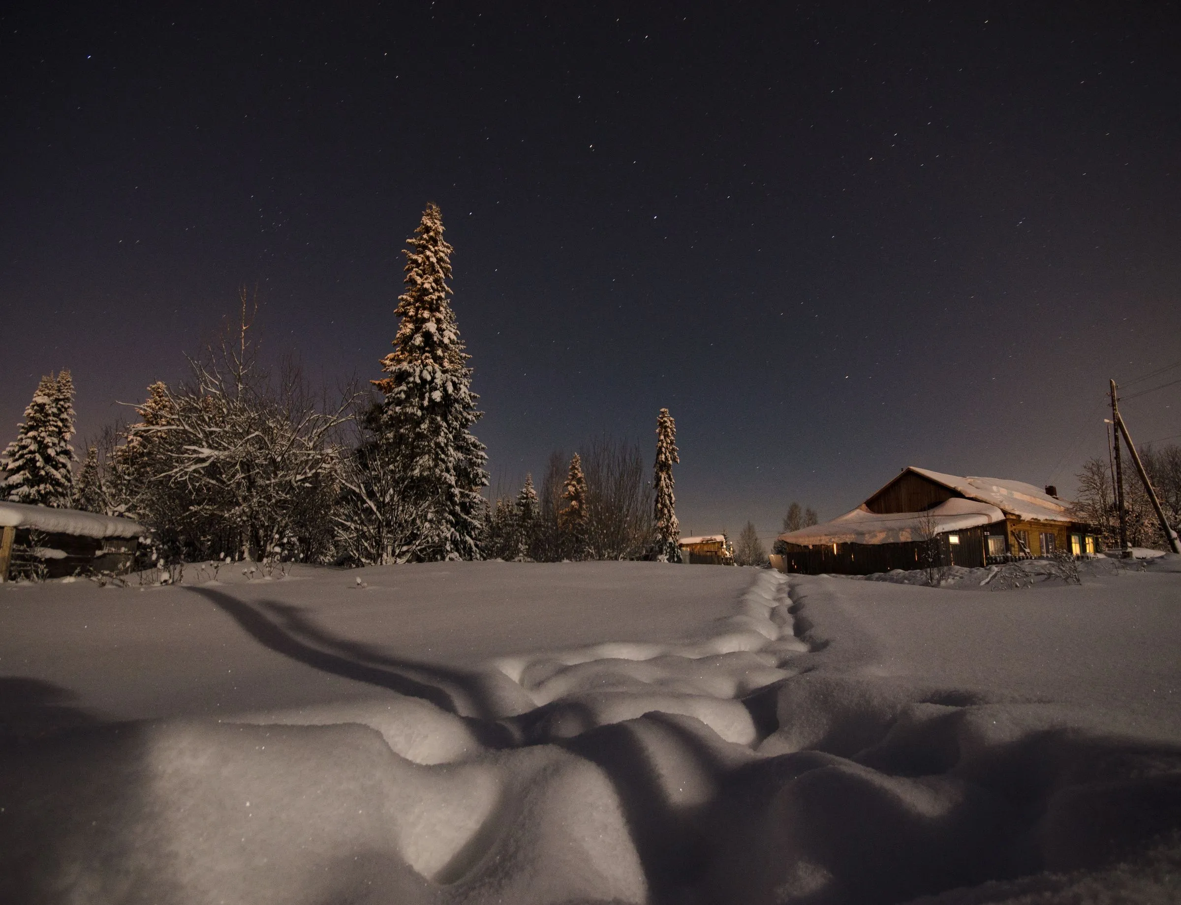 A trodden path through deep snow towards a cabin at night